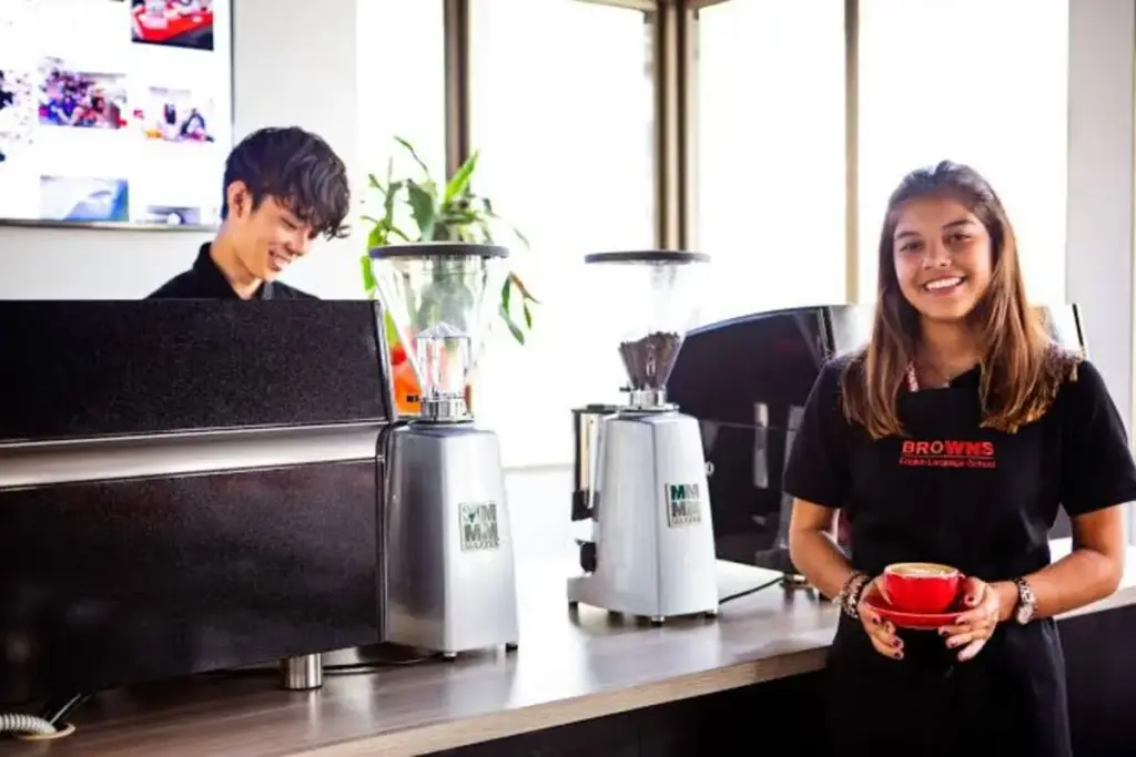 Avustralya'da hizmet sektörü: Bir kafede gülümseyerek kahve sunan kadın barista ve çalışan arkadaşı